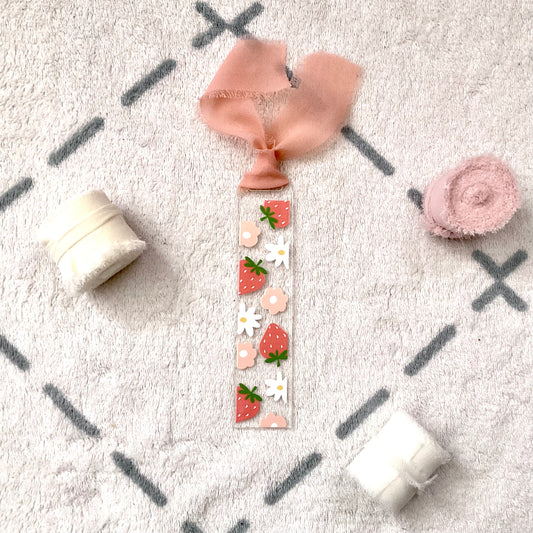 Clear bookmark made of acrylic, we can see through, with red strawberry, white and pink flower. Attached to it is a saumon colour (mix between pink and orange) chiffon ribbon.