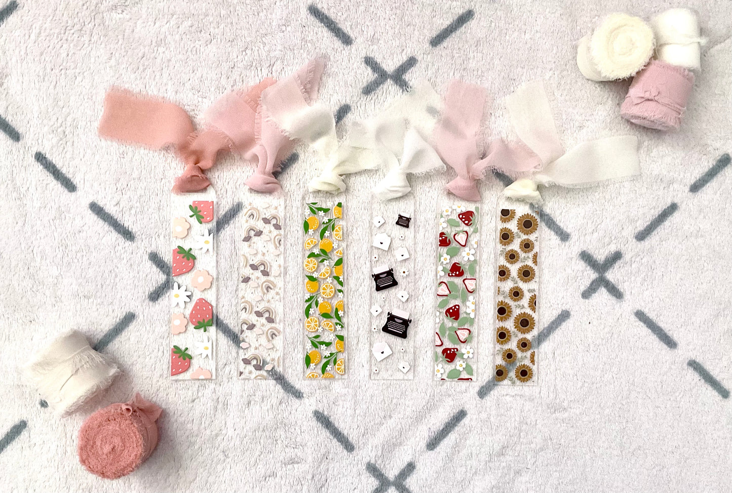 Collection of acrylic bookmark featuring: a strawberry and flower bookmark, a cloud and rainbow bookmark, an oranges and flowers bookmark, a letter and typewriter bookmark, a strawberry and leaf bookmark and a sunflower bookmark. 